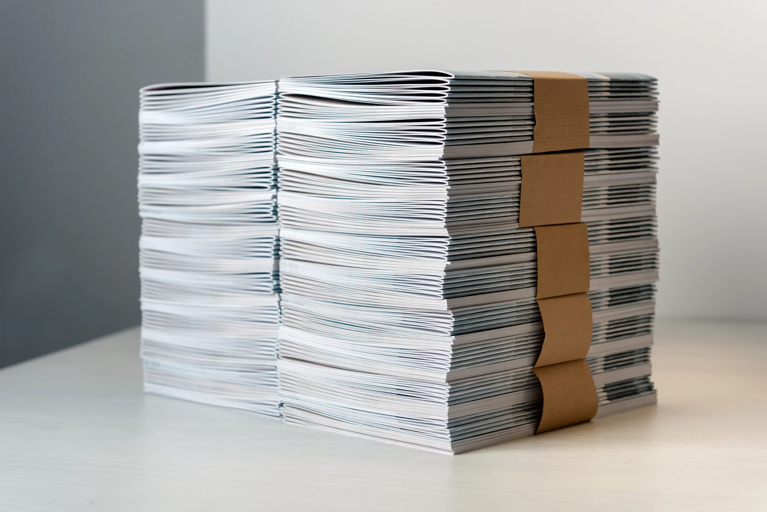 kcopybundles of newly printed catalogues fastened with brown paper arranged neatly in a stack on a white table 2
